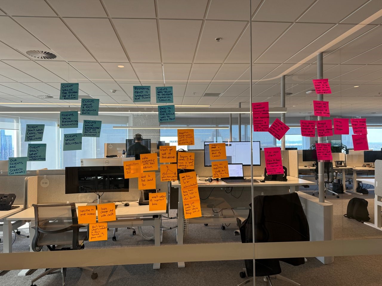 Affinity map of client research insights on sticky notes across an office glass wall